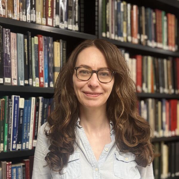 Profile picture of Iona stands in front of book shelves