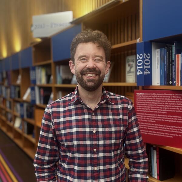 Profile picture of Matt stands in front of the Author's Showcase in Western Bank Library 