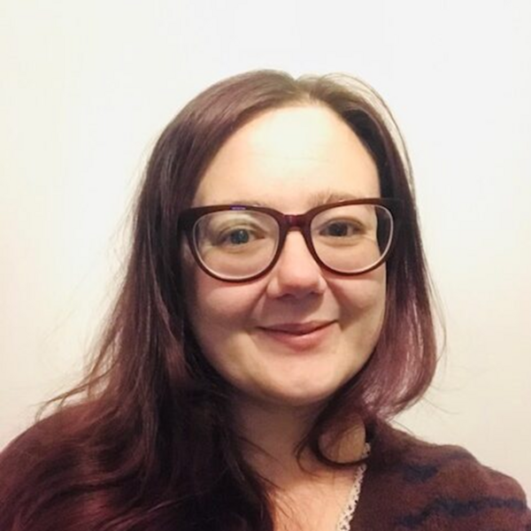 Profile picture of Anna is wearing glasses, with shoulder-length hair, smiling in front of a neutral background