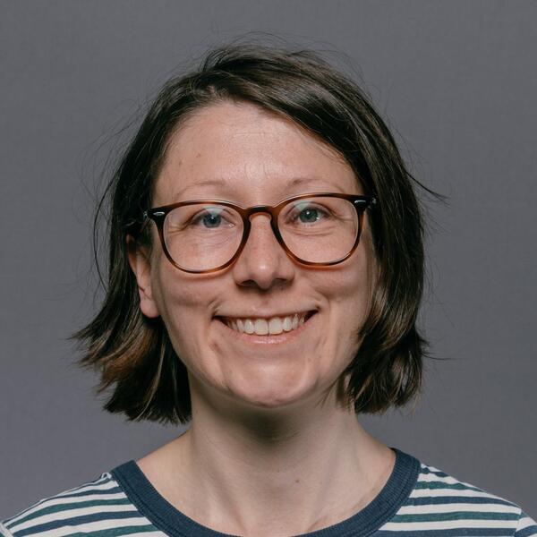 Profile picture of Beth is smiling and wears glasses and a striped top, with chin-length hair, sat in front of a neutral background