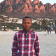 A profile photo of alumni, Saleh. He is wearing a plaid shirt and standing in front of some red rocks. 