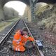 Man on a railway track holding device on the rails in front of bridge