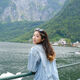 Siqing leans against a metal fence in front of a lake and looks over her shoulder at the camera