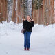 A female student stands on a snowy path with trees lined either side of the path and behind, branches filled with snow. She smiles at the camera and makes a peace sign with both hands.