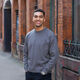 Architecture graduate smiling outside Manchester red brick building in grey jumper and jeans 