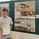 Architecture student holding certificate in front of posters of his work