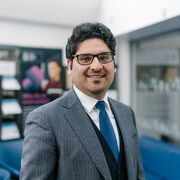 Hossein Olya wearing a white shirt and blue tie, black waistcoat and grey pinstriped jacket.