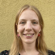 A headshot of Virginia Longo smiling in front of a yellow background