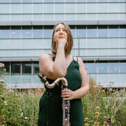 Sarah looks to the foreground, resting her arm on her clarinet.