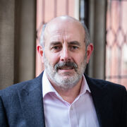 Portrait of a person with a beard, in front of Firth Court windows
