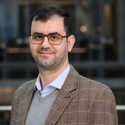 Researcher wearing brown blazer, glasses and smiling