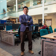 Dr Leslie Ing stands arms crossed in a busy office space