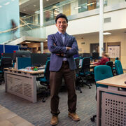 Dr Leslie Ing stands arms crossed in a busy office space