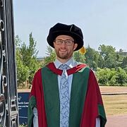 Liam Hughes, a white male, stands wearing graduation gown, hood and cap