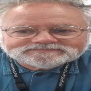 Michael faces the camera directly, wearing a blue shirt and glasses, with short hair and a beard.
