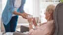 A carer hands an elderly person a cup of tea