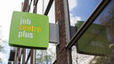 Picture of the Job Centre Plus sign attached to a building. The sign is green with white and yellow text.