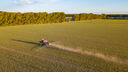 Aerial view of a farm tractor in a yellow field during spraying and for growing food, vegetables and fruits on indian summer sunny day. Agriculture industry.