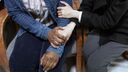 Two people comfort eachother on waiting room chairs, holding hands
