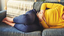 A picture of a woman laid on a sofa clutching her stomach in pain.