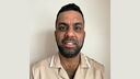 Gurpreet smiling at the camera wearing his apprentice nursing uniform.