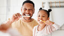A father and daughter look in the mirror as they brush their teeth