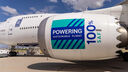 a large white jet plane, with the engine in the foreground. The engine has the world '100% SAF powering sustainable flight' written on it