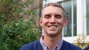Profile photo of Jude Stone, head and shoulders of smiling man with short grey hair wearing a blue jumper outside a building.