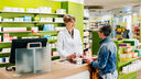 A lady speaking to a pharmacist at the counter of a well stocked chemist 