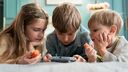 Three children playing with a hand held gaming device