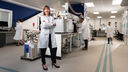 Dr Karen Finney wears a lab coat and stands with arms crossed in a lab