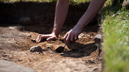 A close up of hands using a trowel to uncover soil at a dig site.