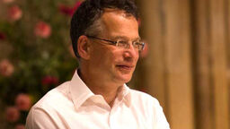 A photograph of Professor Bob Stern. He wears a white shirt and there are pink flowers behind him.