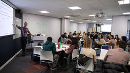 A lecture taking place in the School of Health and Related Research. The lecturer points at a presentation.