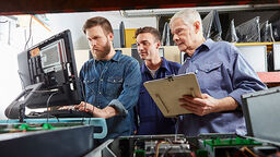 Three men of different ages are working in front of a computer.