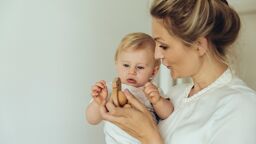 A Mother holding a child, showing them a wooden toy