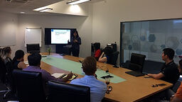 Dr Gate Pichawadee Kittipanya-ngam giving a talk in front of a screen to a group of people sat around a table.