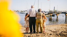 Grandparents and grandchildren with their backs to the camera, looking out at a harbour