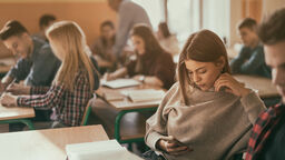 A photograph of a school classroom. Student looks at her phone.