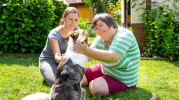A picture of two people sat on the grass stroking a dog