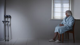 A picture of an elderly woman seated alone, out of reach of crutches