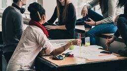 A group of people sat round a table working together. On the table is stationery and papers.