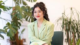 Image of Politics alumni and Sky News Journalist, Olive Enokido-Lineham, in a green suit sat by plants