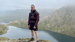 Bradley stood in a mountainous area in front of a river or lake
