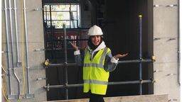 A woman in a yellow hi-vis vest and wearing a white safety helmet.