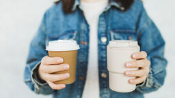 A person holding one disposable coffee cup and one reusable coffee cup