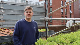 A white man stands outside next to some green plants