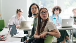 A photo of two students sat by their laptops listening to a lecturer in a seminar