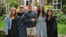 five students with arms around each other pose in against a garden backdrop. 