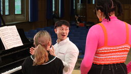 Students talking around a piano 